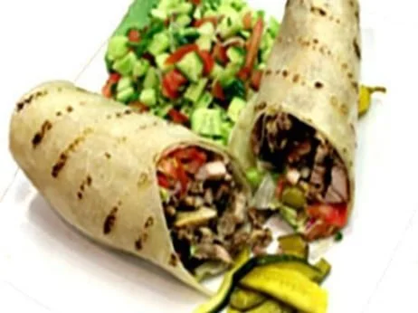 Two beef burritos with grilled marks, sides of chopped lettuce, tomatoes, and pickles.