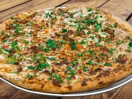 A large pizza topped with cheese, chopped herbs, and diced tomatoes.