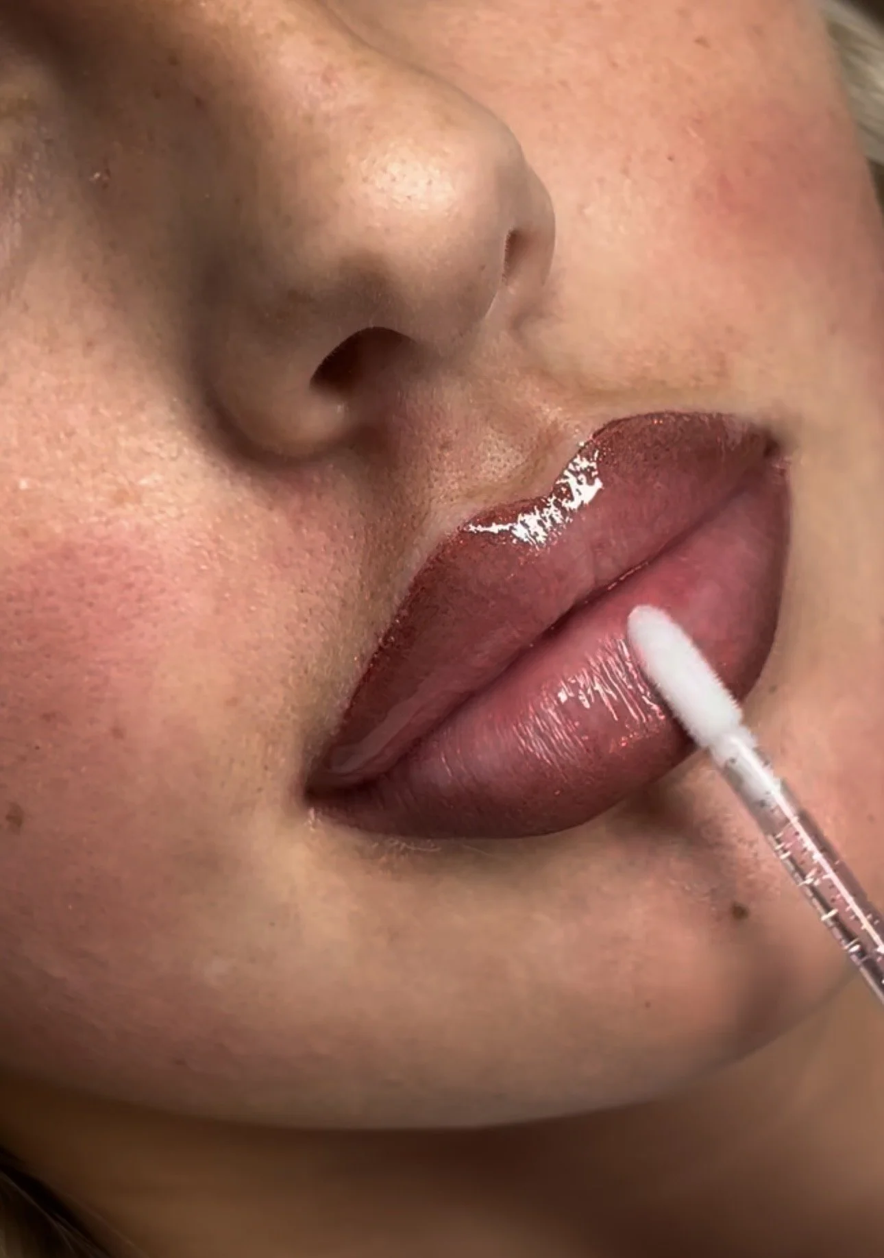 Close-up of a person applying lip gloss with a cotton swab.