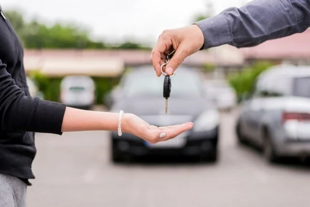 Person handing over car keys to another person in a parking lot.
