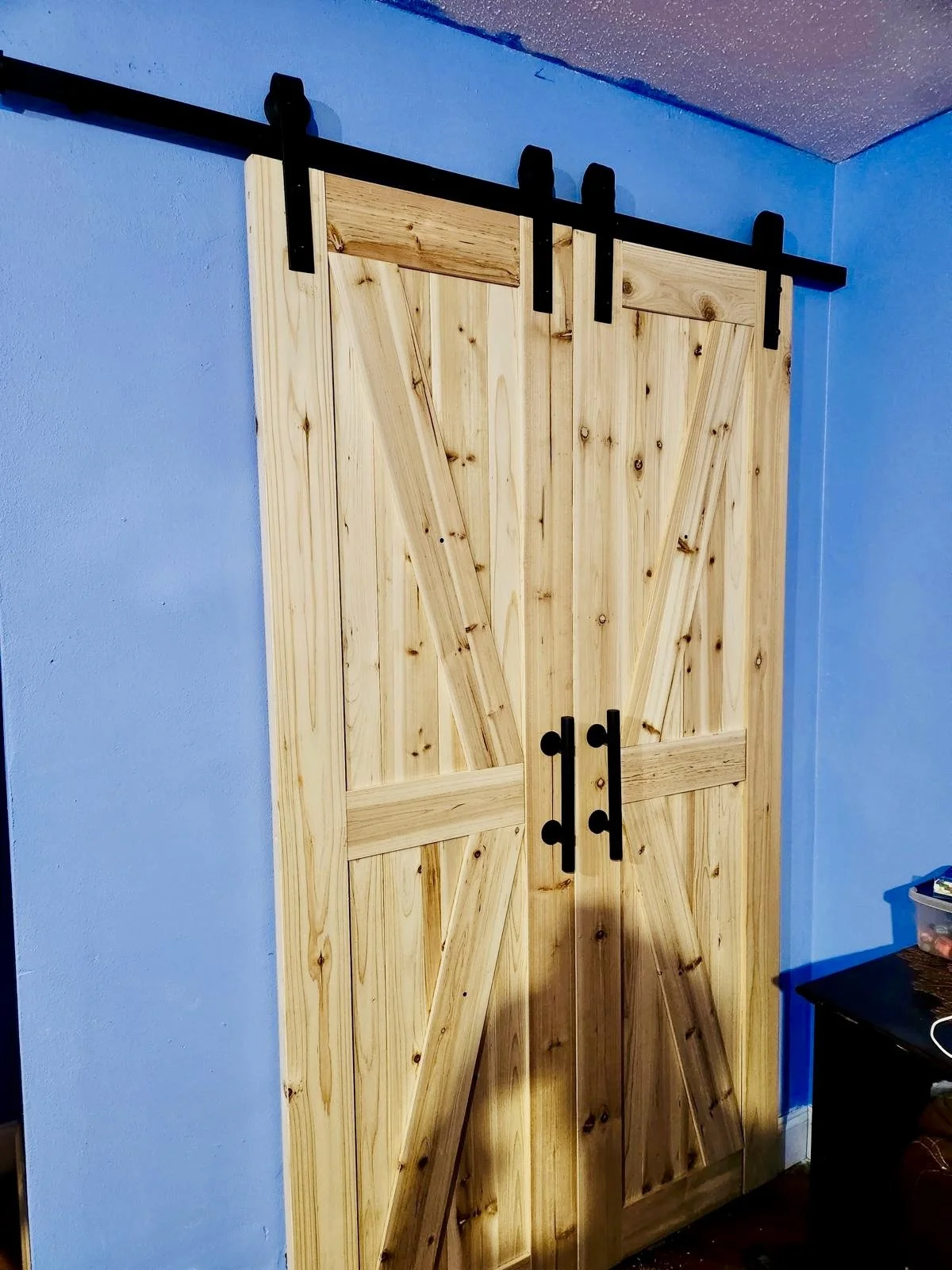 A wooden barn-style sliding door with black hardware, installed inside a room with blue walls.