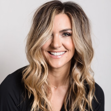A smiling Nicole Sciacca of Sweat + Stillness with long, wavy blonde hair wearing a black top.