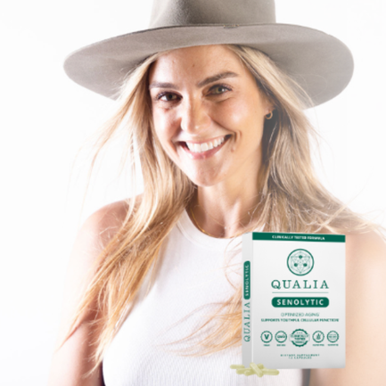 Nicole Sciacca of Sweat + Stillness wearing a large wide-brimmed hat and sleeveless white top, holding a package of QUALIA Senolytic supplement.