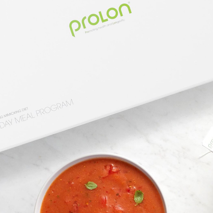 A bowl of PROLON tomato soup with basil leaves on top, placed in front of a white box with green and gray text.
