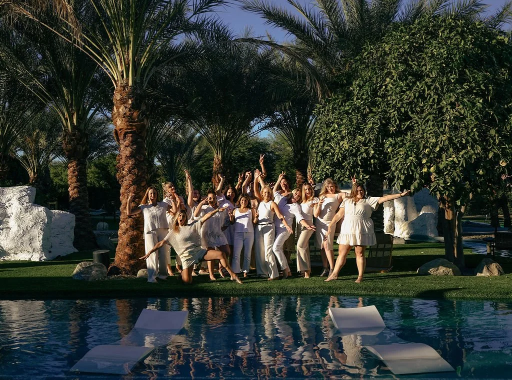 Retreat Photo: Group of women dressed in white posing by the pool and palm trees at sunset with Nicole Sciacca of Sweat + Stillness