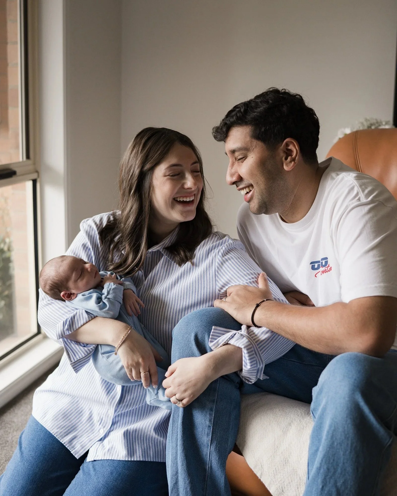 New parents sharing a smile while cuddling their newborn baby at home during a newborn photography session in Bentleigh, Melbourne.