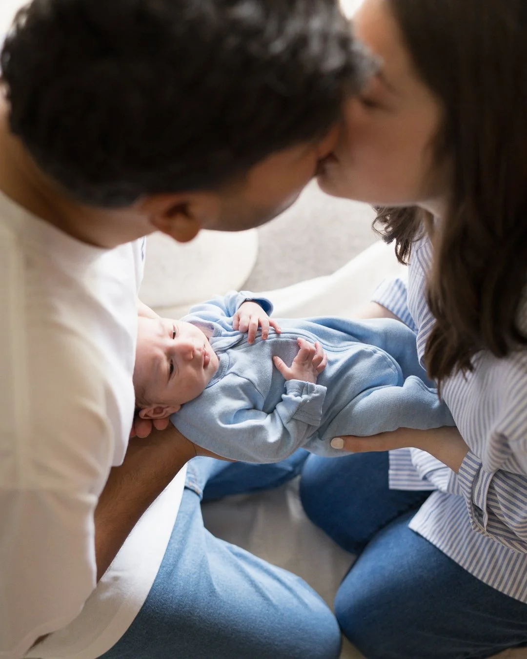 Parents sharing a kiss while holding their newborn baby during a relaxed in-home lifestyle newborn photography session in Bayside,Melbourne.