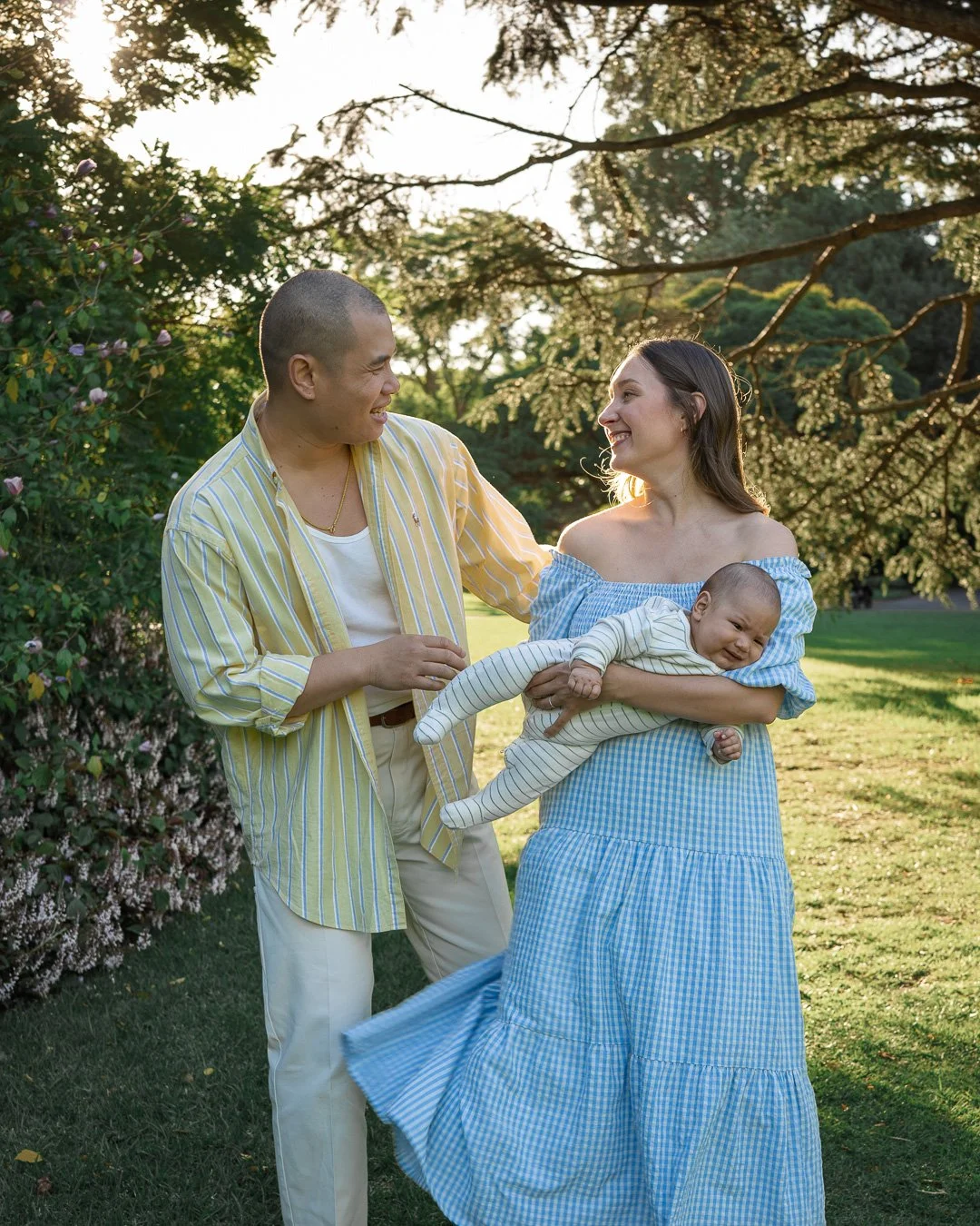 Parents smiling at each other while cradling their baby during an outdoor family photography session at the Royal Botanic Gardens Melbourne.