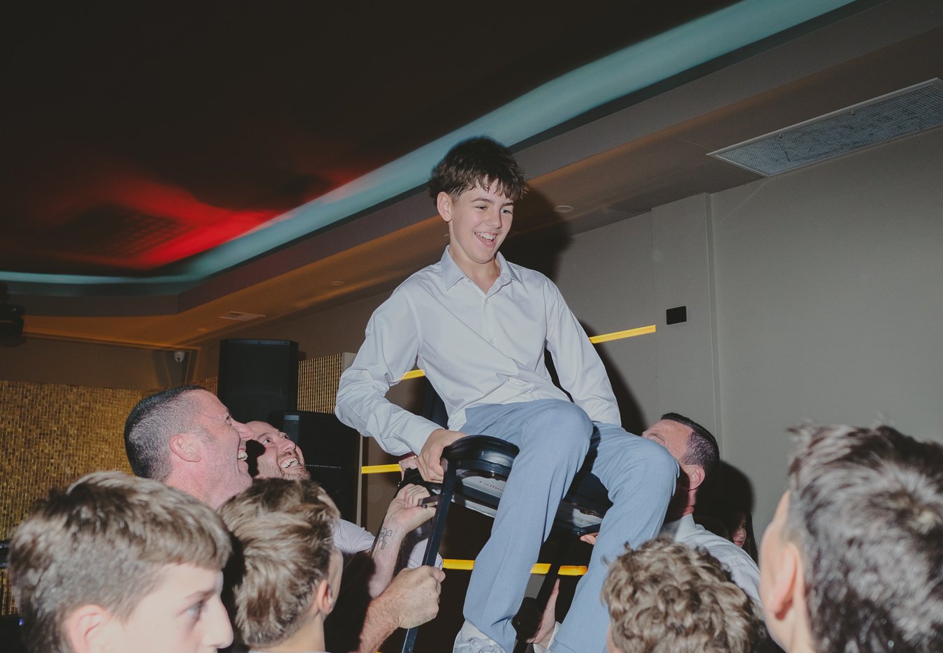 Family and friends lifting the Bar Mitzvah boy on chairs during the celebration in Bentleigh.