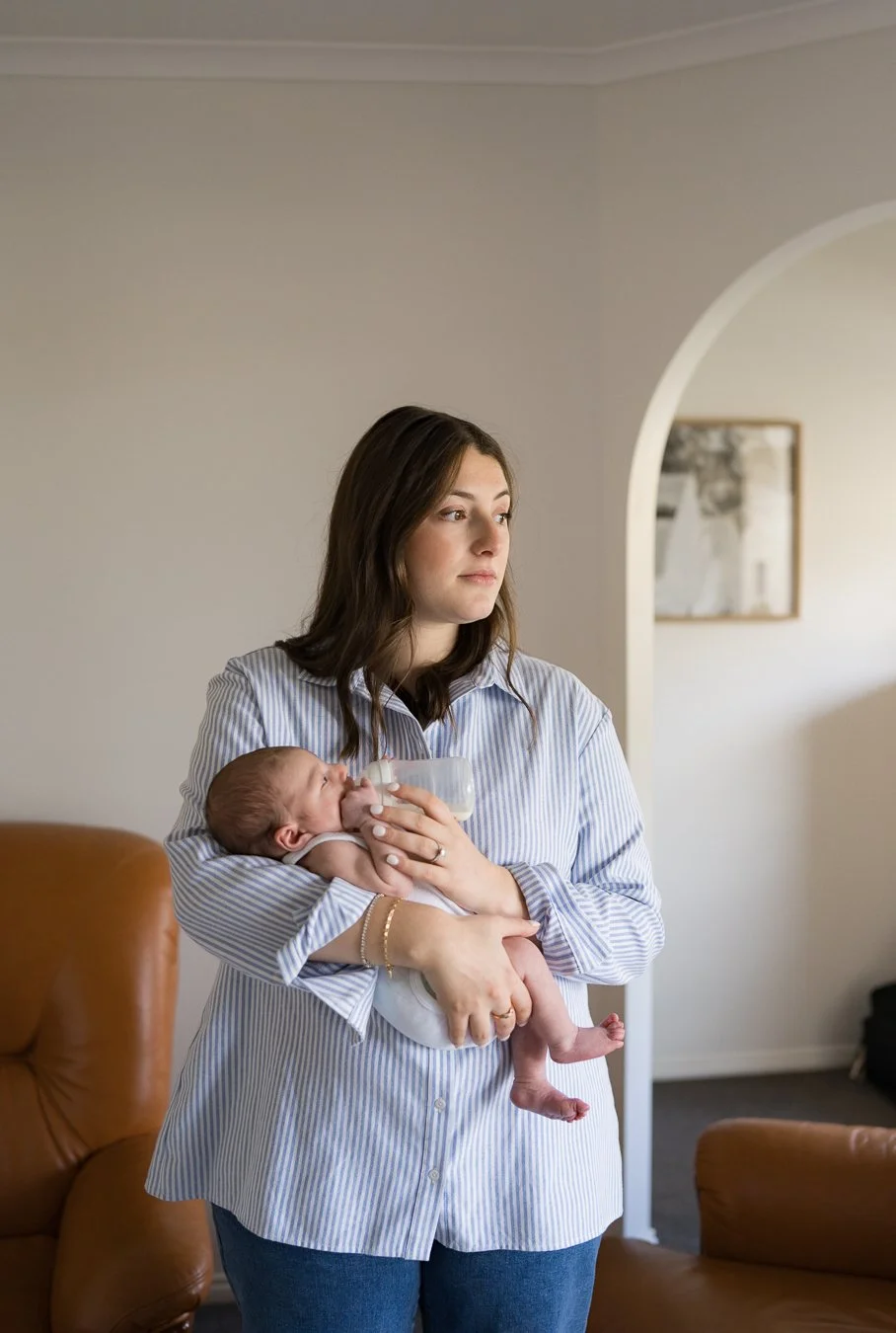 New mother feeding her newborn baby during an in-home lifestyle newborn photography session, capturing a quiet everyday moment in Melbourne.