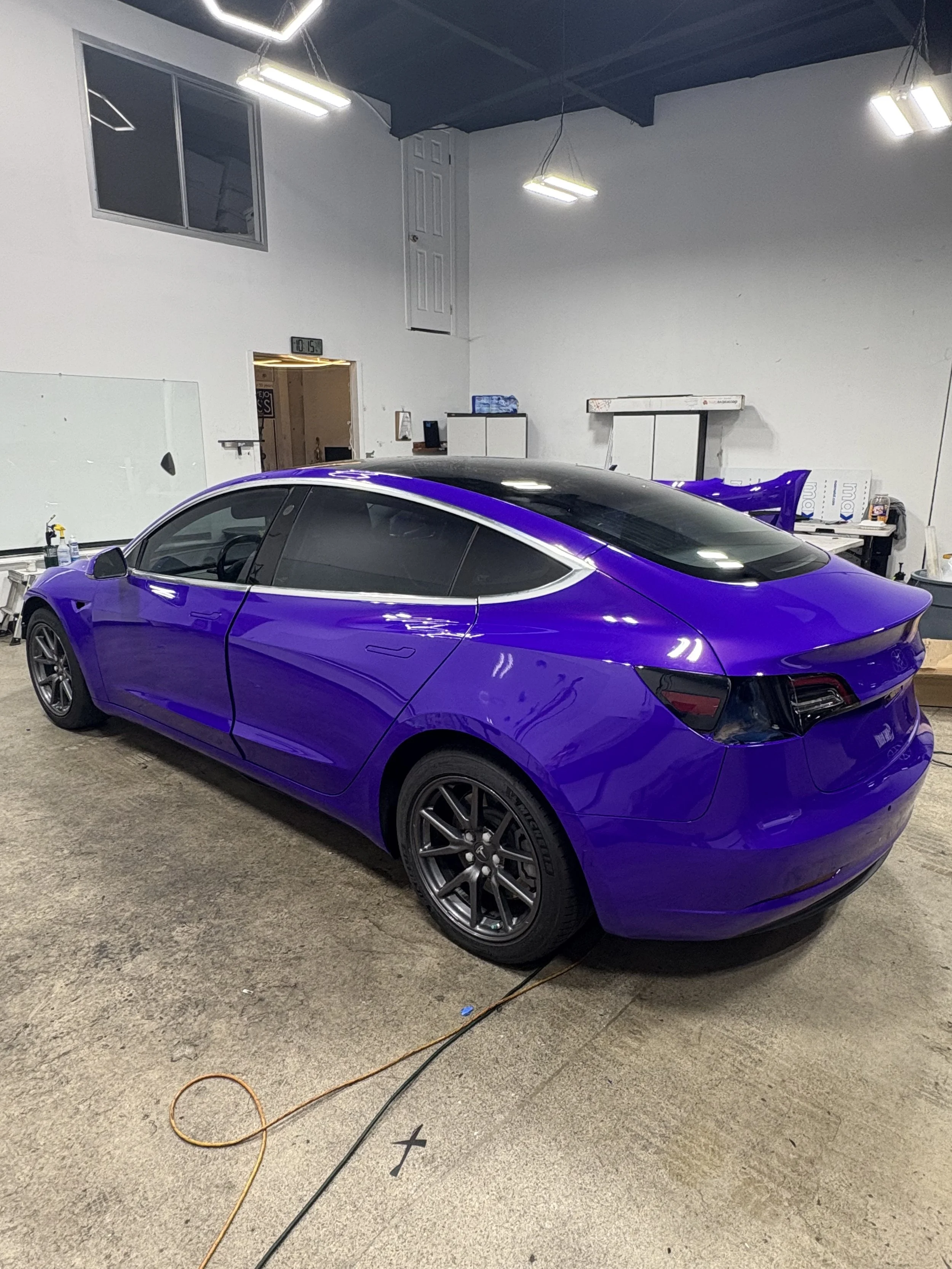 A purple Tesla Model S parked inside a garage with tools and equipment around it, and a whiteboard on the wall.