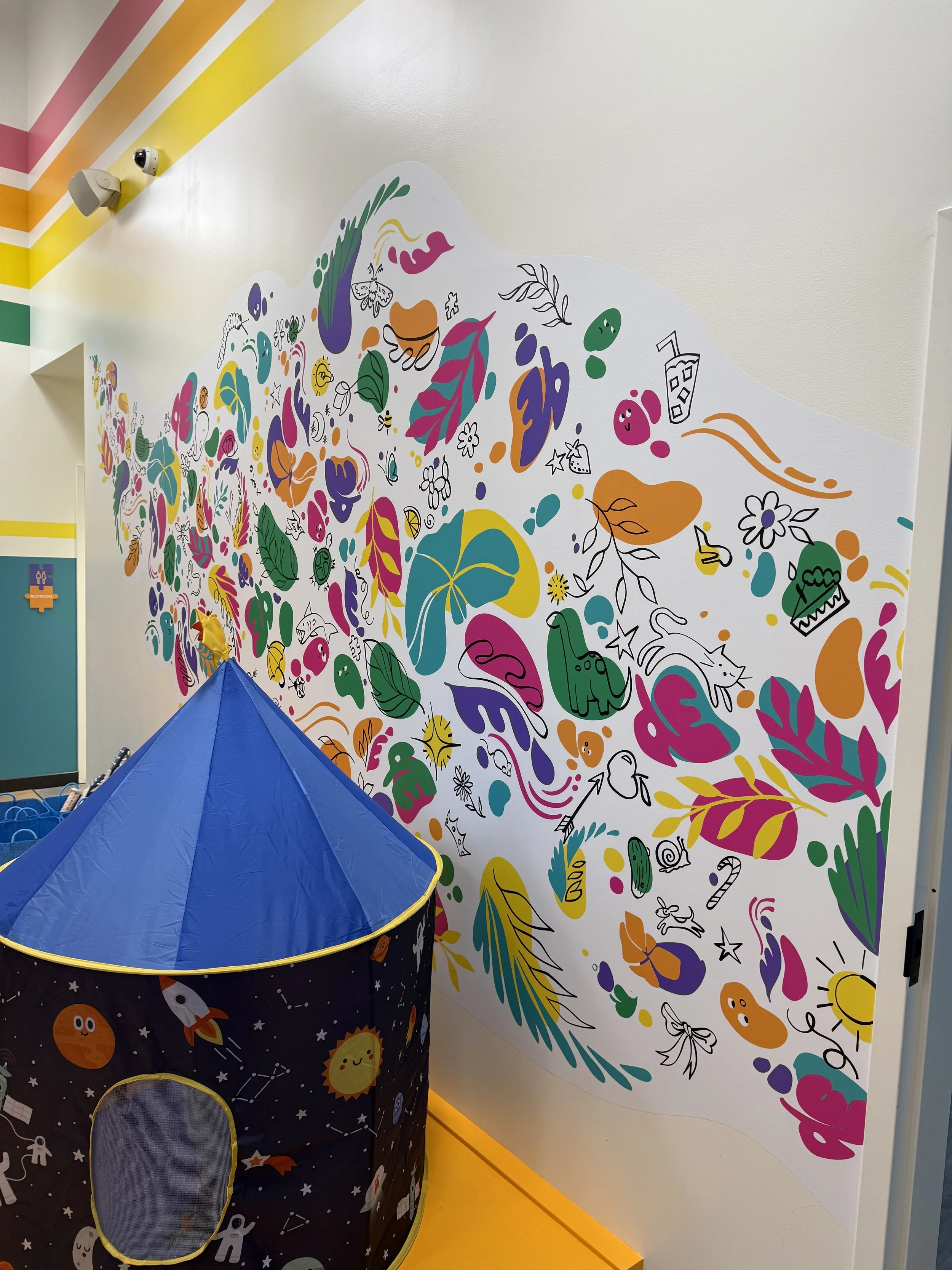 Indoor scene with a colorful mural wall featuring playful illustrations and a blue pop-up tent.