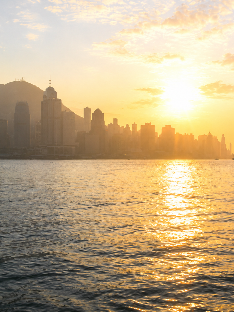 Sunrise over Victoria Harbour in Hong Kong, with the skyline reflected on the water.