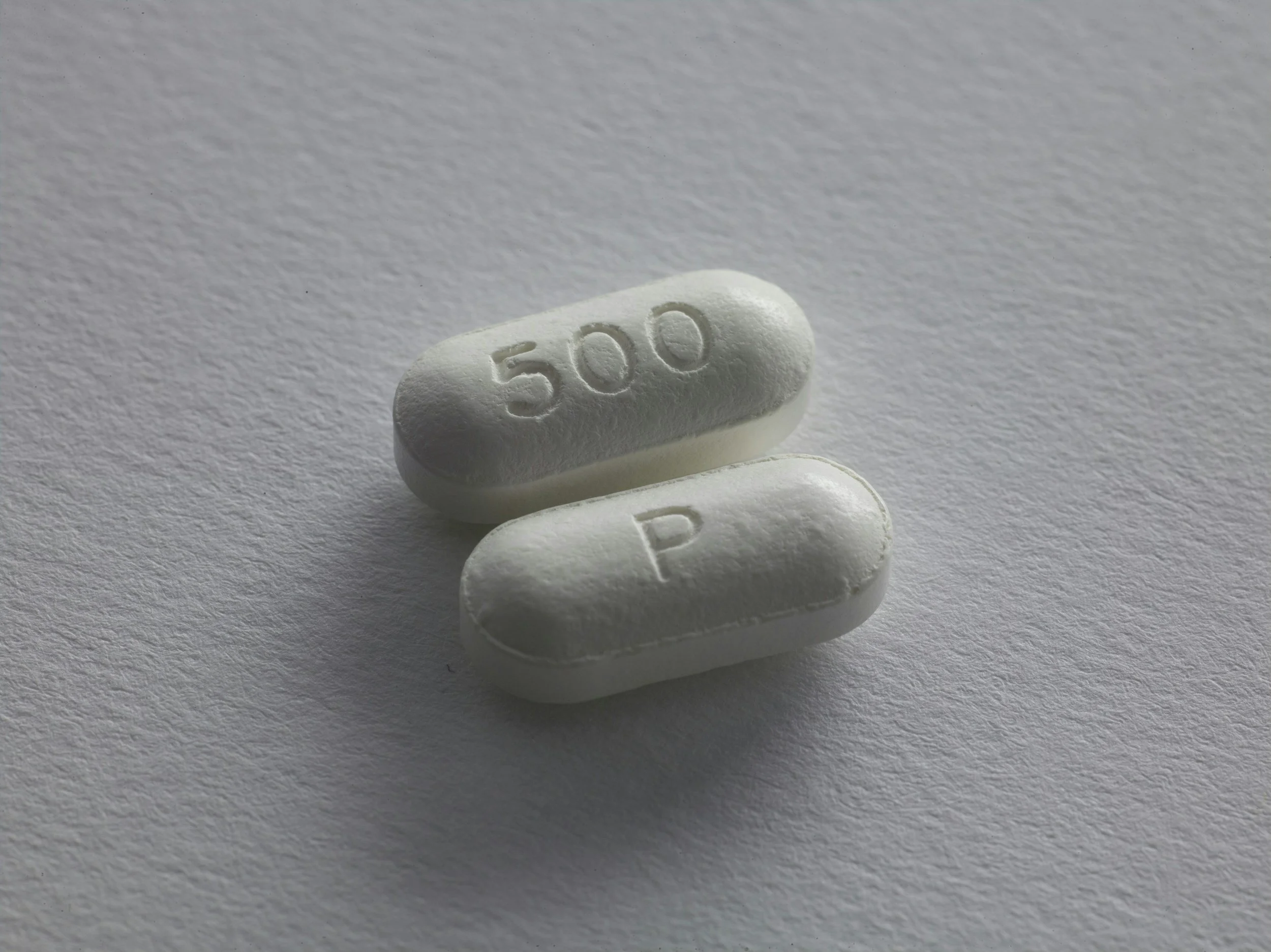 Three white pills stacked on top of each other with the number '500' embossed on the top pill, placed on a white textured surface.