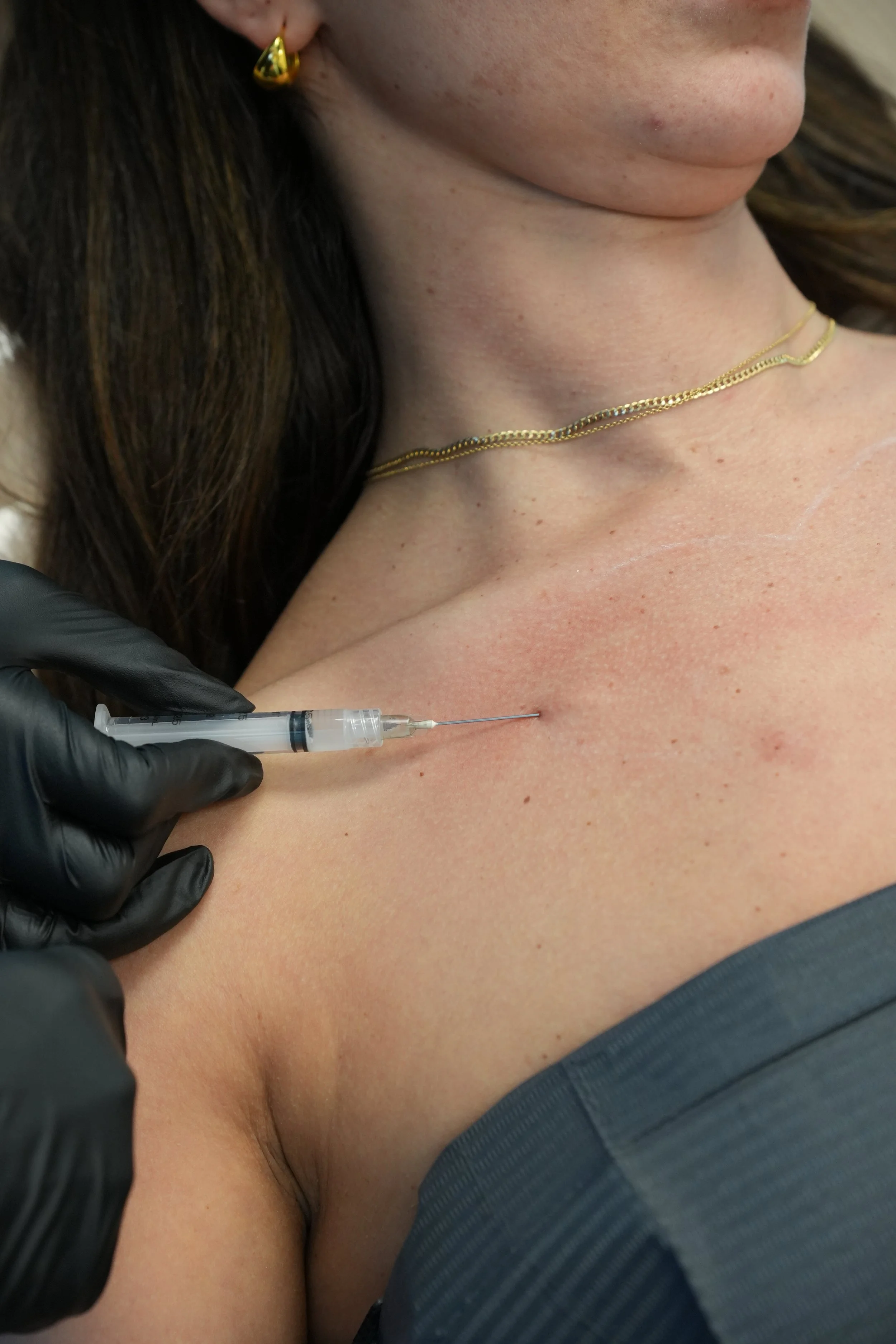 A person receiving a vaccination shot in their upper arm from a healthcare professional wearing black gloves.