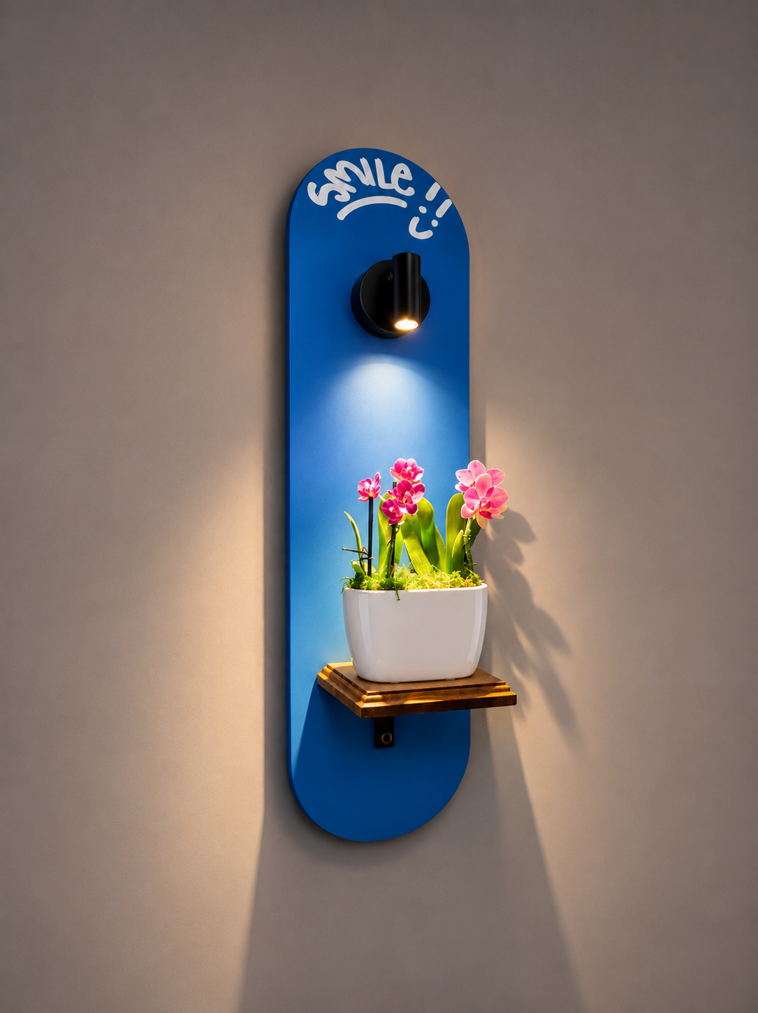 A wall-mounted light fixture with a blue backplate with the word 'smile' and a smiley face, illuminating a white flower pot with pink orchids on a small wooden shelf.