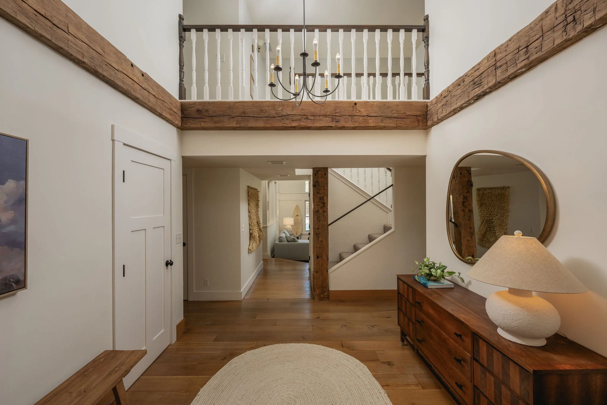 Interior view of a home with wooden beams, a black chandelier, a round mirror, and a console table with a lamp and plant