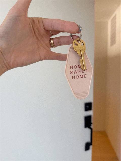 Person holding a key with a pink keychain that says 'Home Sweet Home' on a white background.