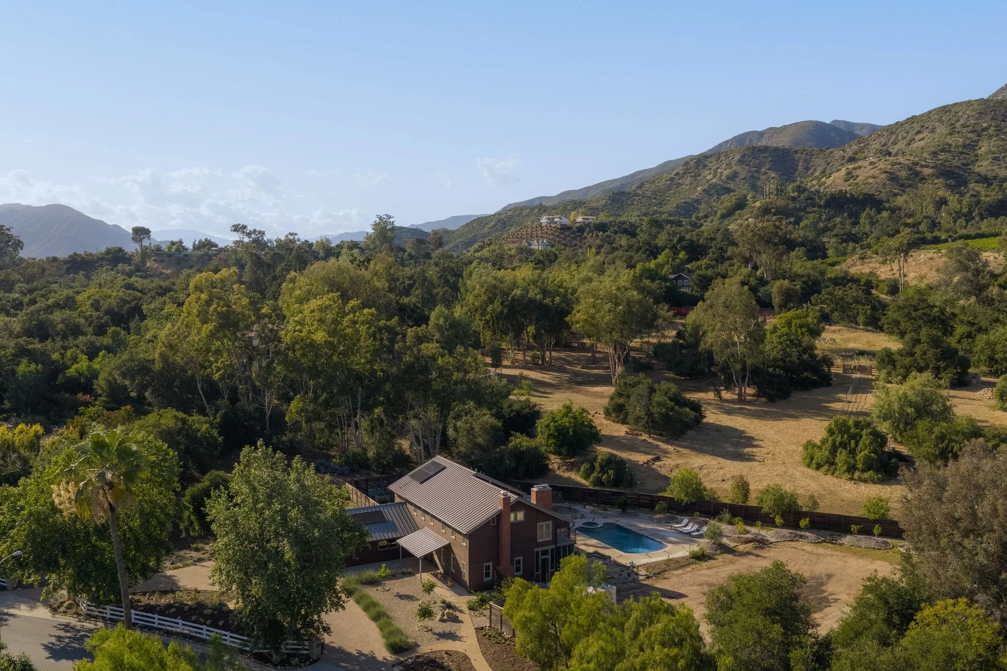 A house with a backyard swimming pool located in a hilly, green landscape with trees and mountainous terrain in the background.