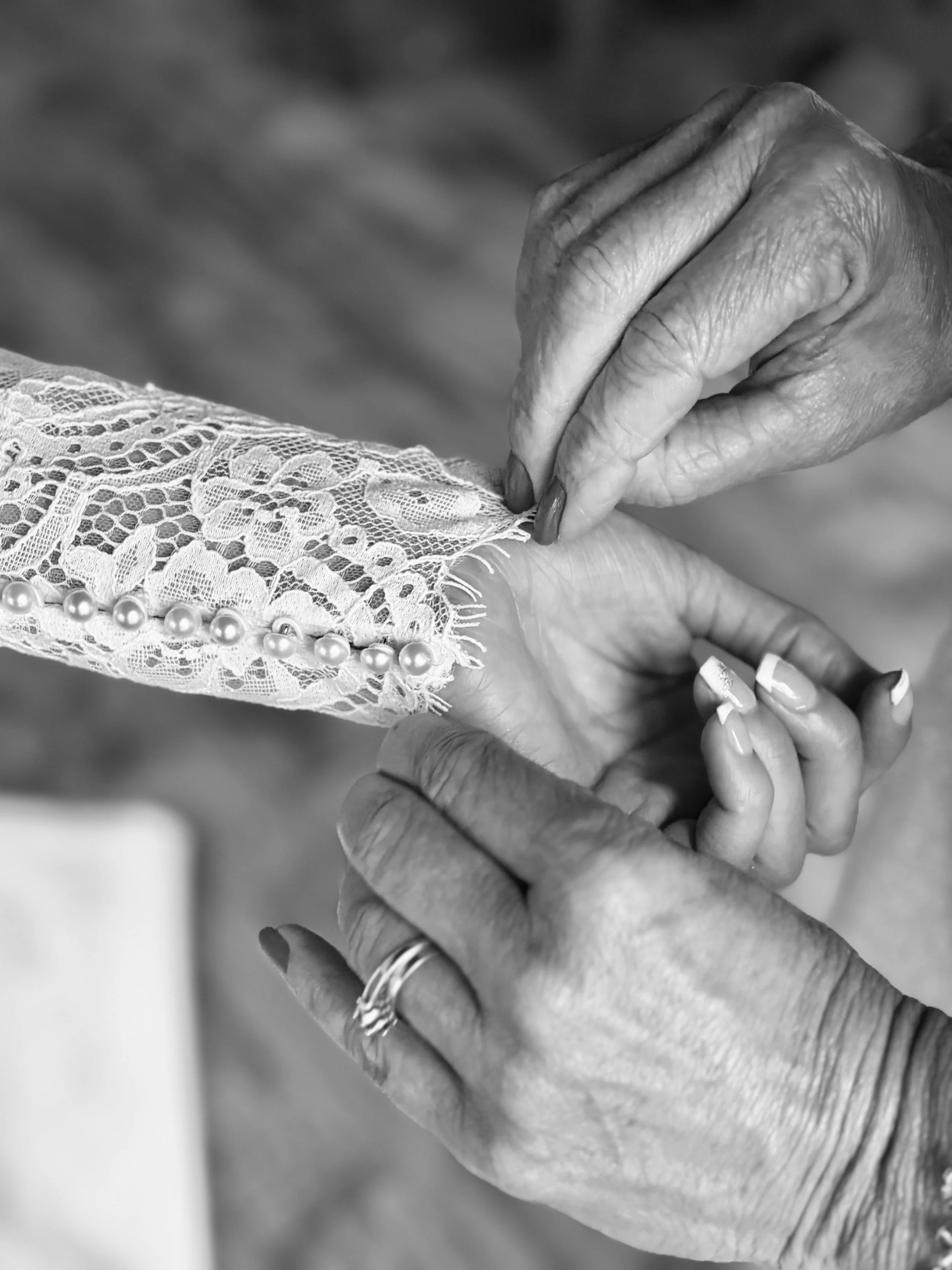 Close-up of an elderly person holding a lace-gloved hand with pearl bracelet, showing detailed hand and jewelry.