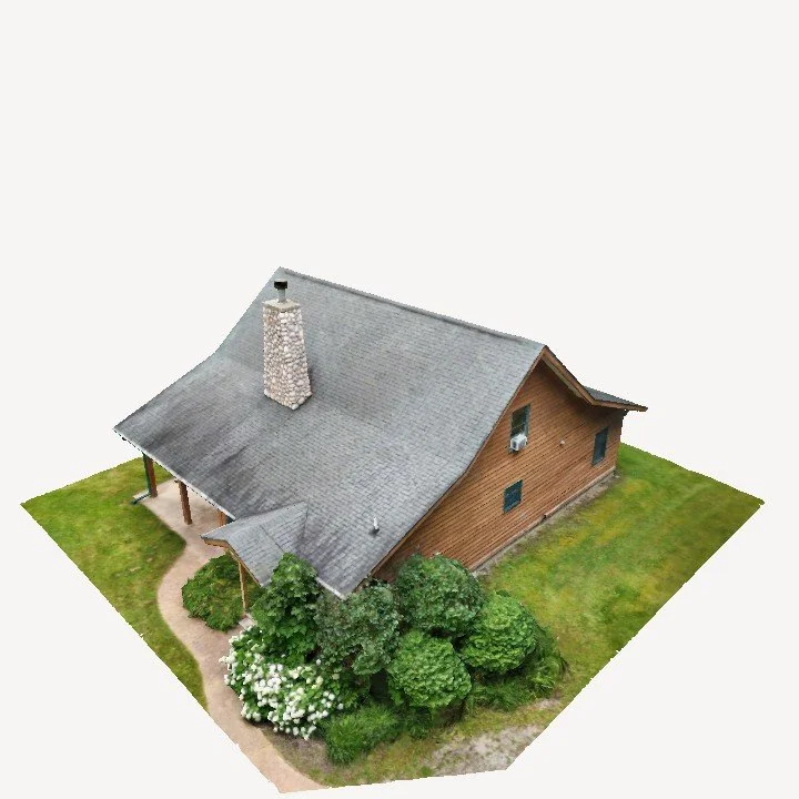 Aerial view of a suburban house with a gray roof, brick chimney, and small front yard with bushes and trees.