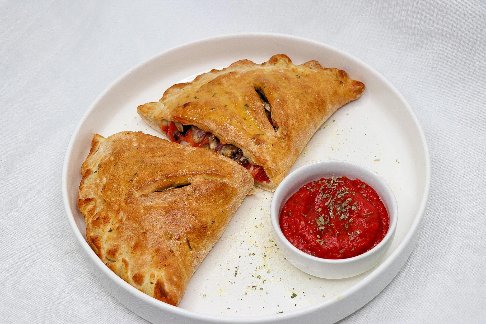 Two golden-brown baked spring rolls on a white plate with a side of marinara sauce garnished with herbs.