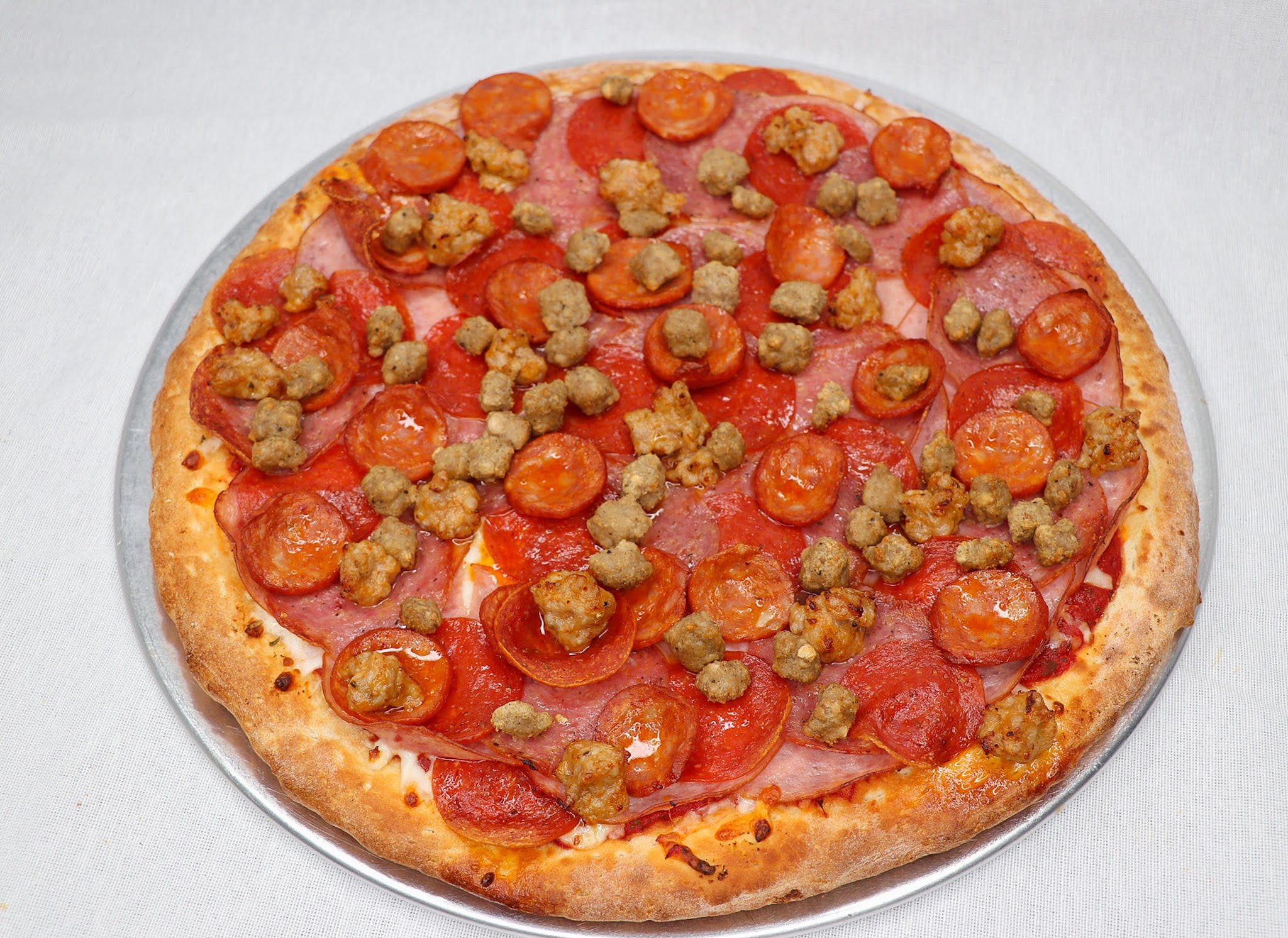 A pizza topped with pepperoni, sausage, ham, and cheese on a white surface