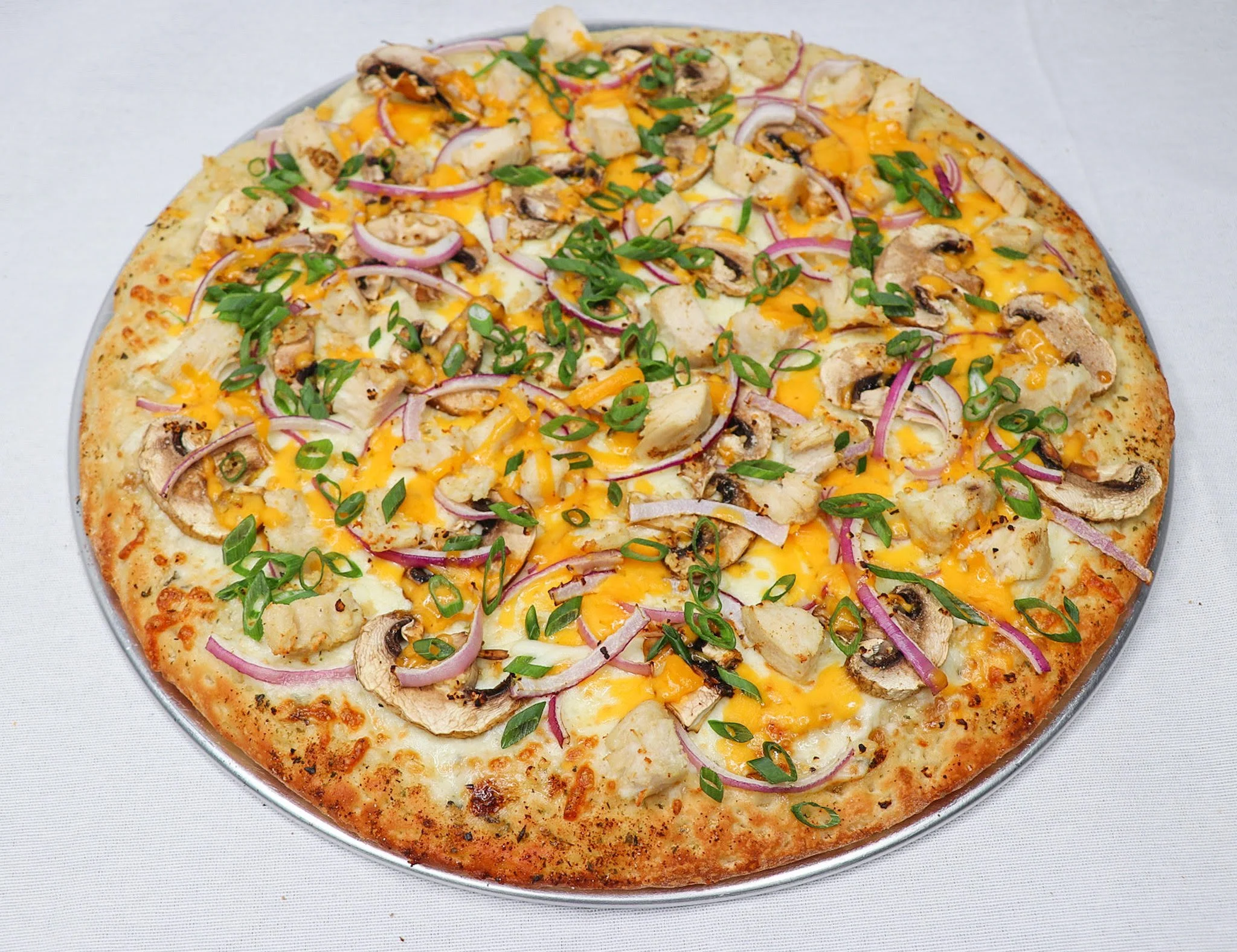 A pizza topped with cheese, mushrooms, red onions, cooked chicken, and chopped green onions on a silver platter.