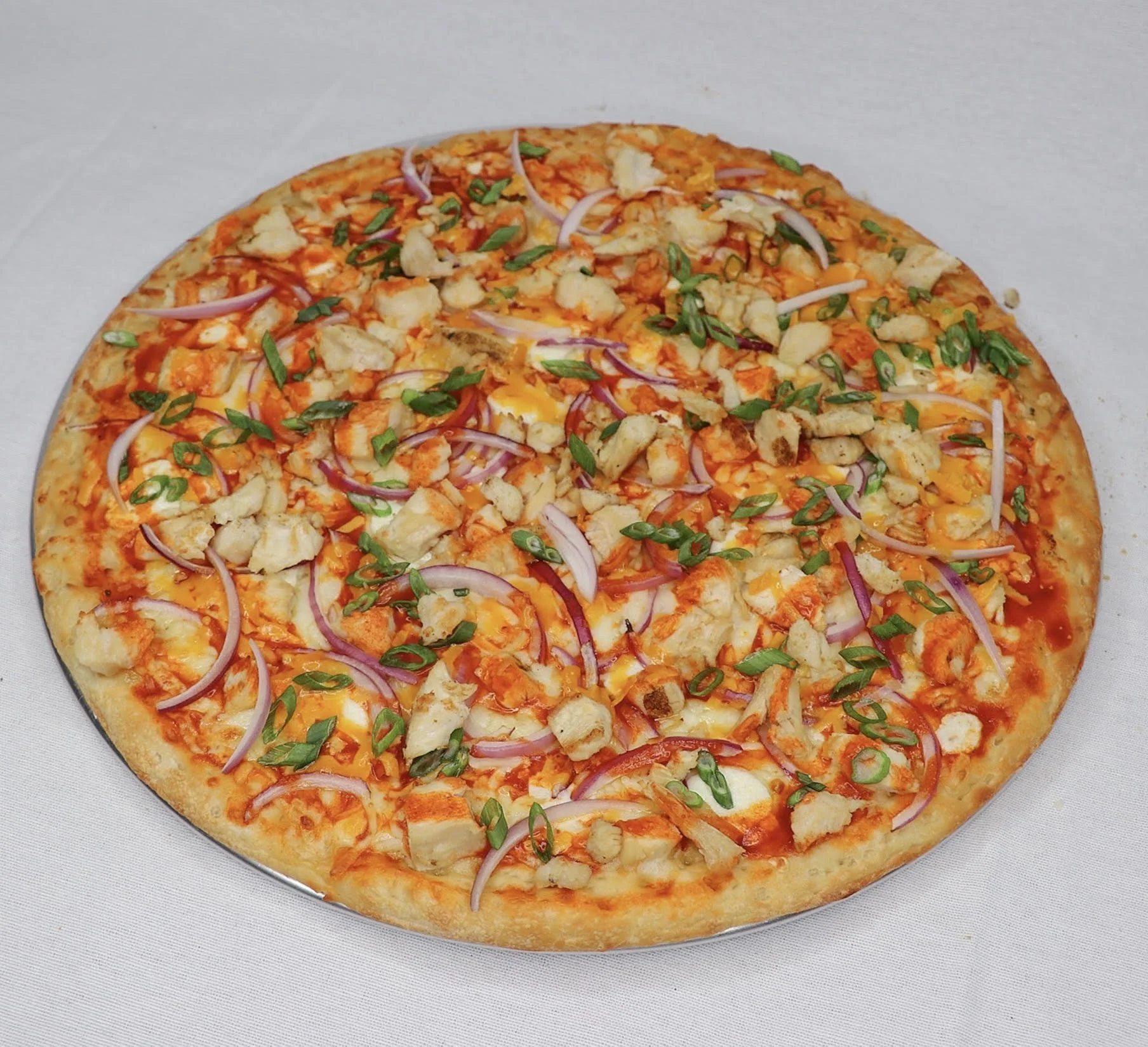 A pizza with toppings of grilled chicken, sliced red onions, cheddar cheese, green onions, and cheese on a baked crust.