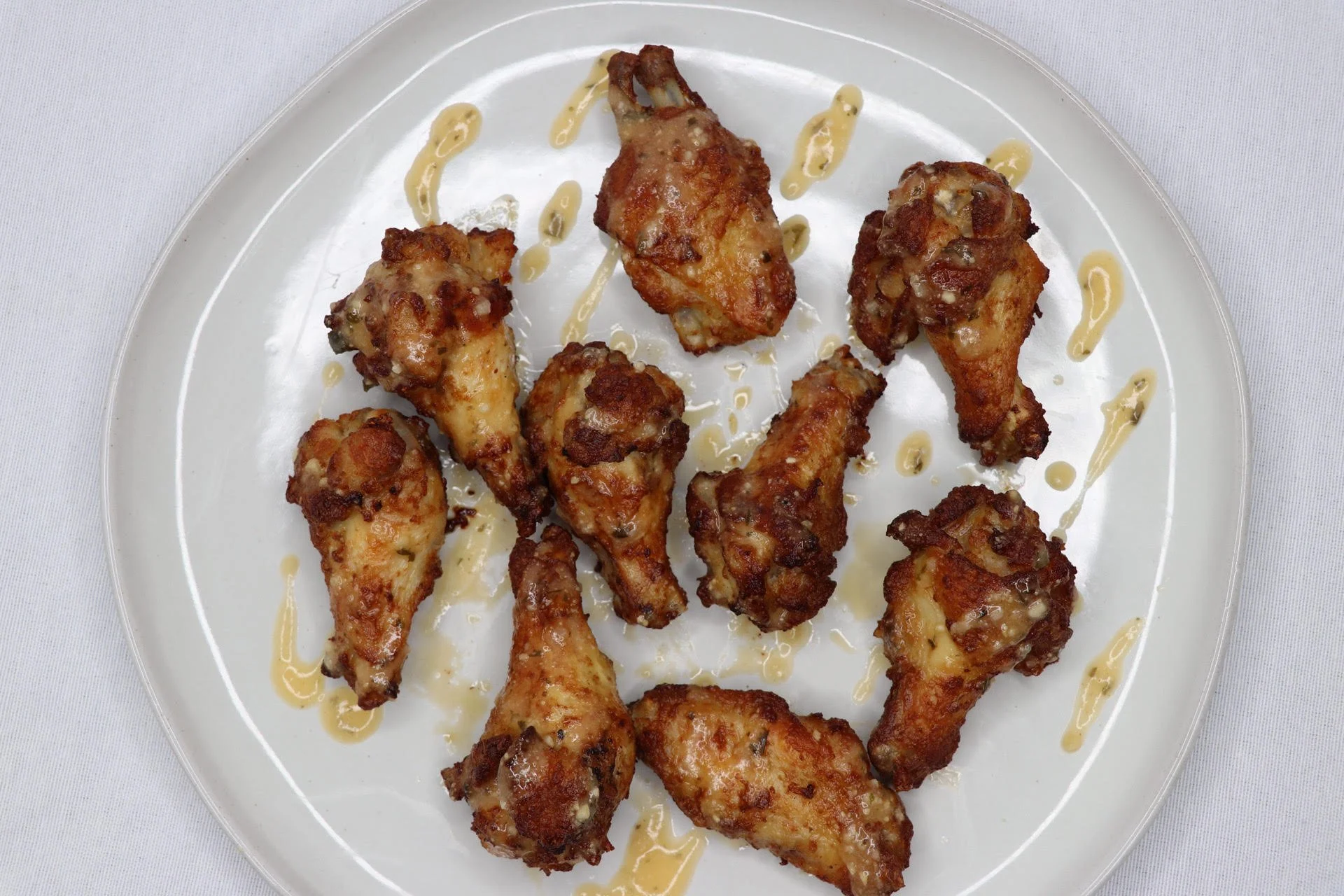 A white plate with several fried chicken drumsticks drizzled with a light-colored sauce, set against a white background.