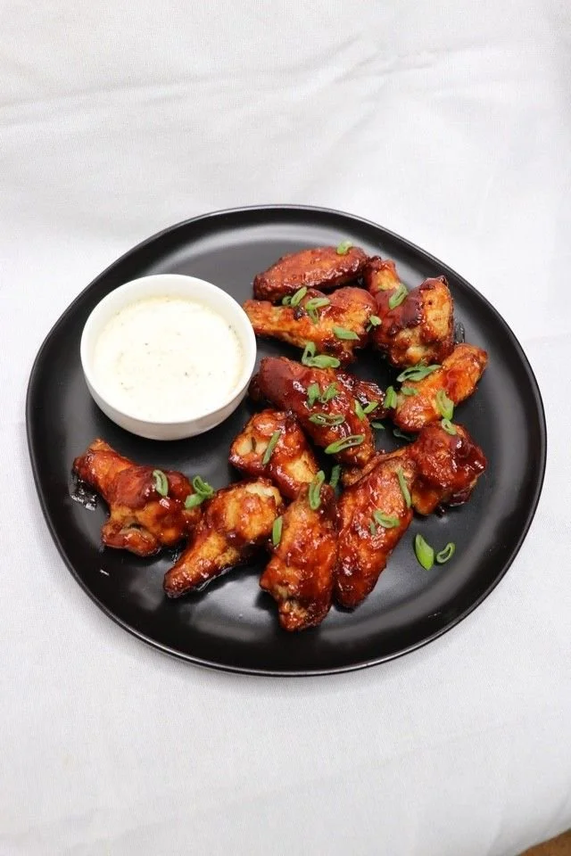 Plate of buffalo chicken wings garnished with green onions, served with a side of creamy dipping sauce.