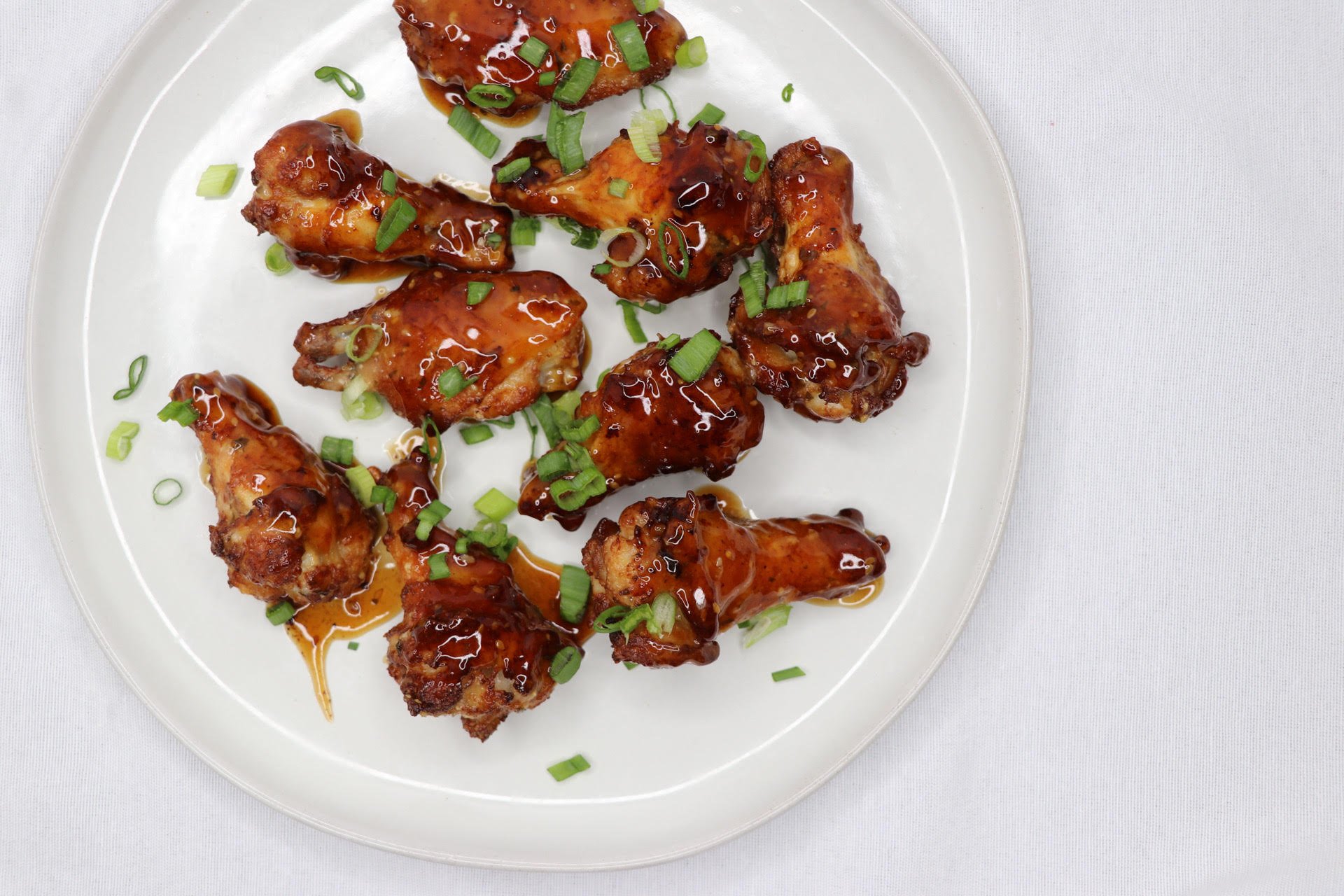 Plate of glazed chicken wings garnished with chopped green onions on a white plate