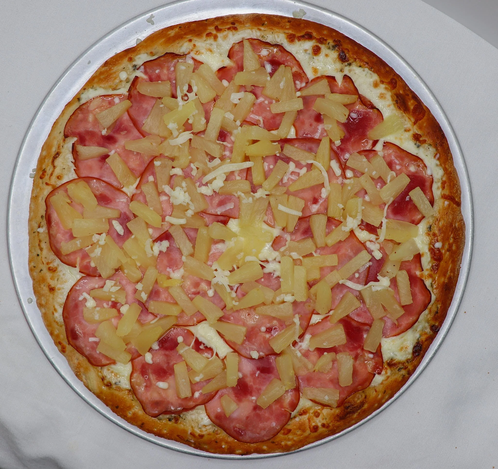 A pizza topped with pineapple chunks, slices of ham, and shredded cheese on a silver tray.