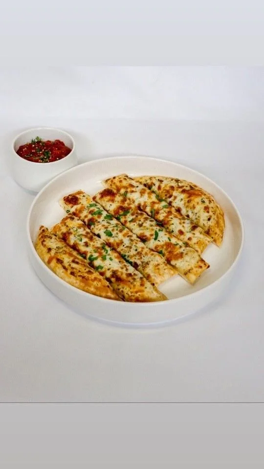 A white plate with several slices of cheesy garlic bread garnished with chopped green herbs, accompanied by a small bowl of marinara sauce on a white background.
