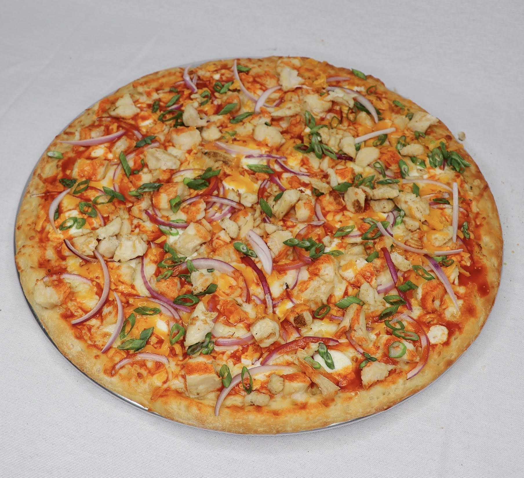 A whole cheese pizza topped with pieces of chicken, sliced red onions, chopped green onions, and melted cheese on a silver tray.