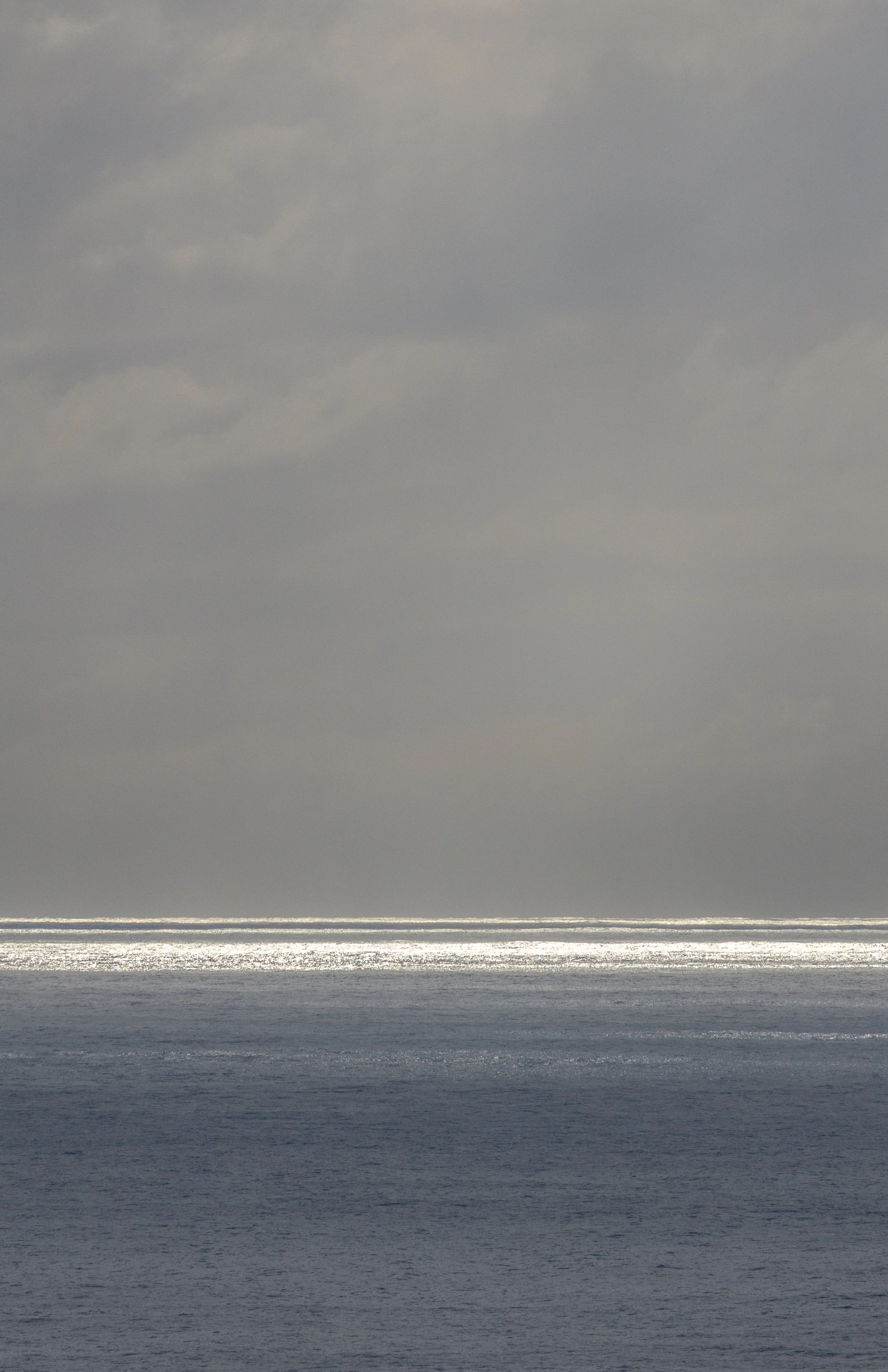 Dark cloudy sky over an ocean or large body of water with shimmering light reflections on the surface.