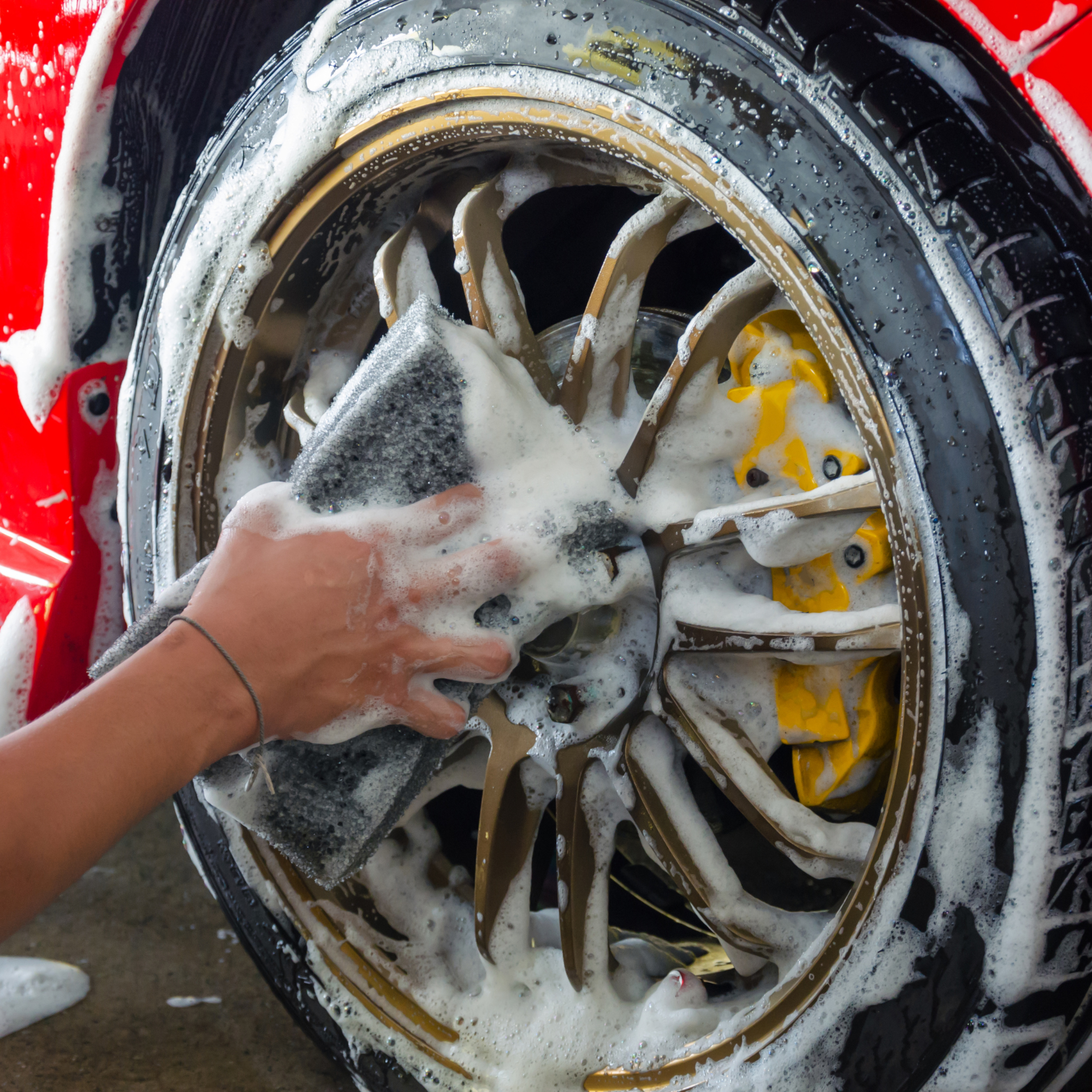 Close-up of a washing machine drum with soap suds and a person's hand inside, cleaning off foam.