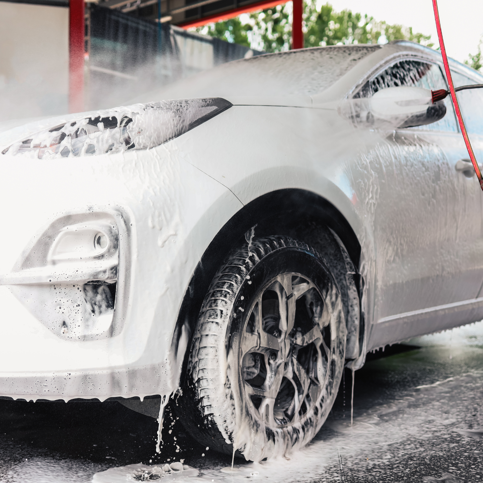 Black tires on a car being washed with foam and water during a car wash.