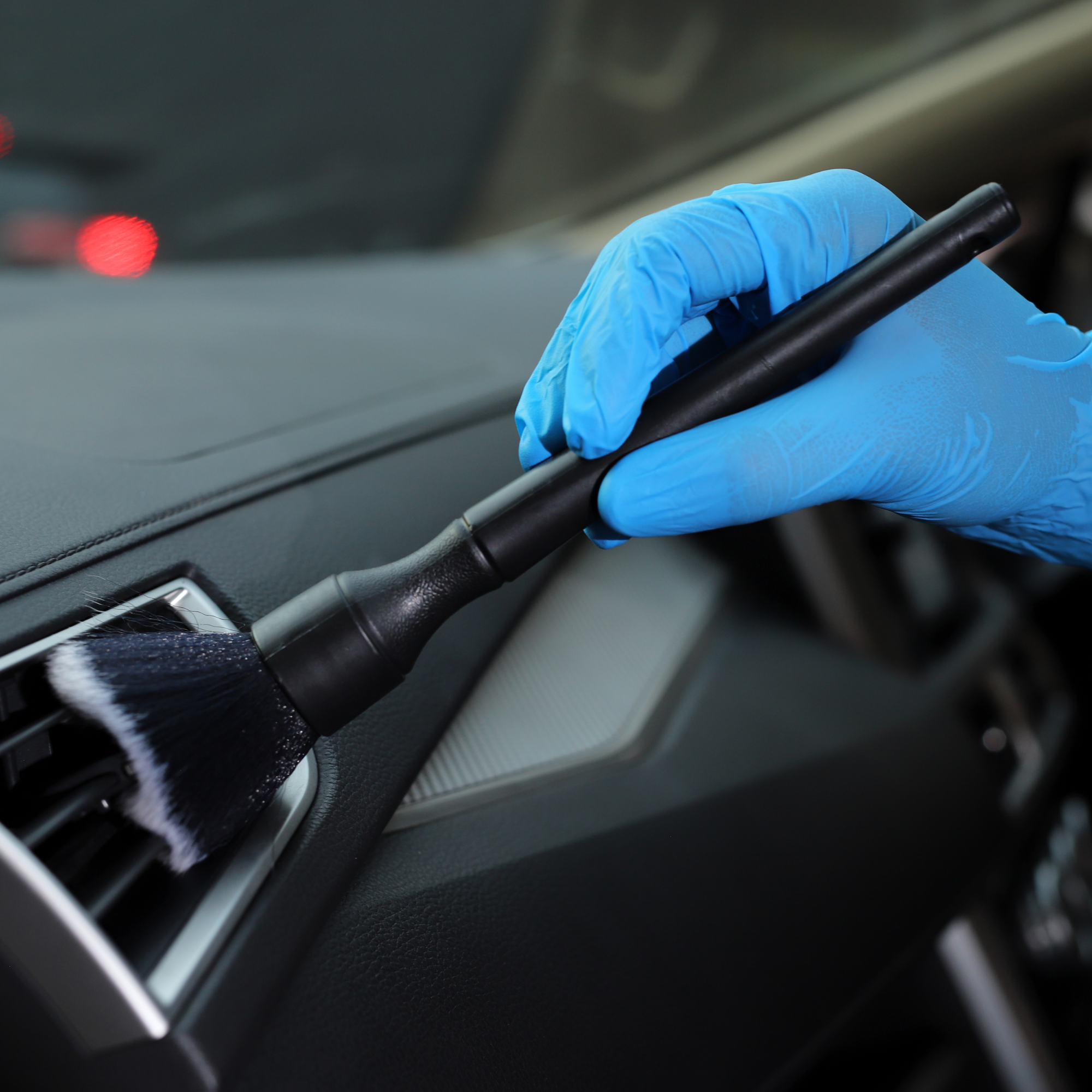 Close-up of a gloved hand holding a small screwdriver near a car dashboard air vent.