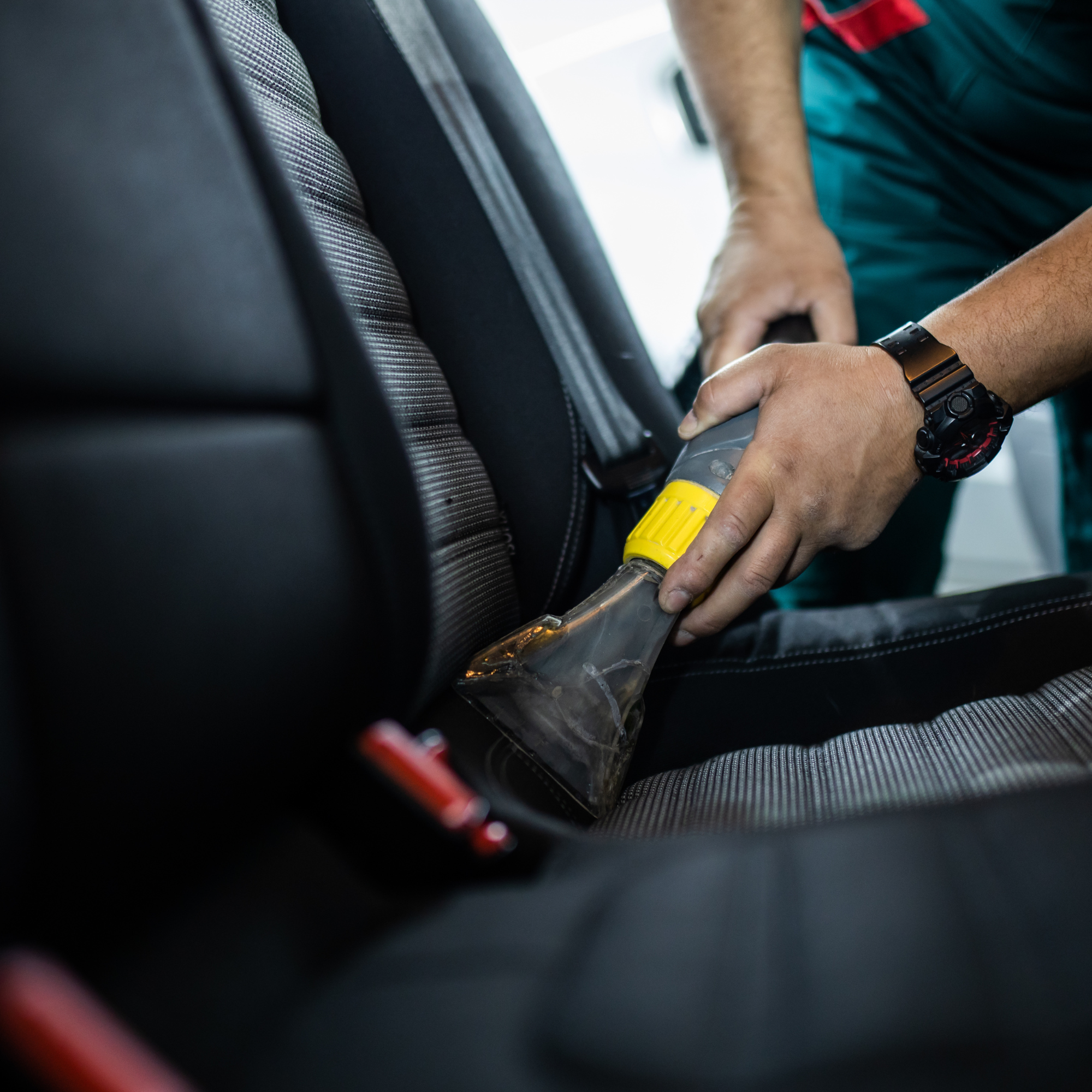 Close-up of a person wearing a black watch, holding a tool with a yellow handle, working on a surface inside a vehicle, with the focus on their arm and hand.