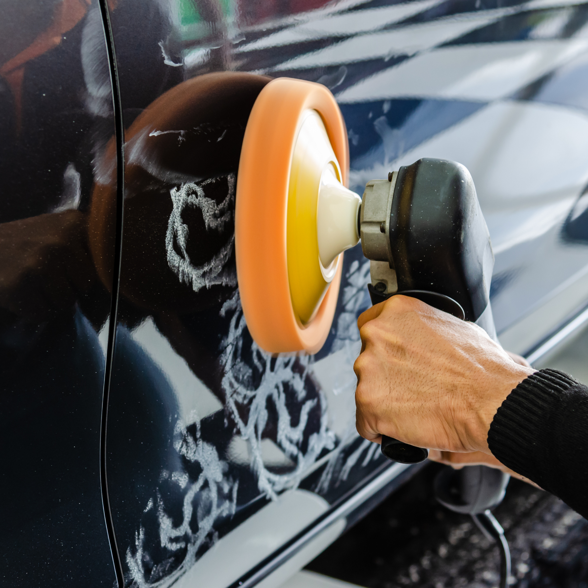 Person polishing the side of a black car with a yellow and orange buffer