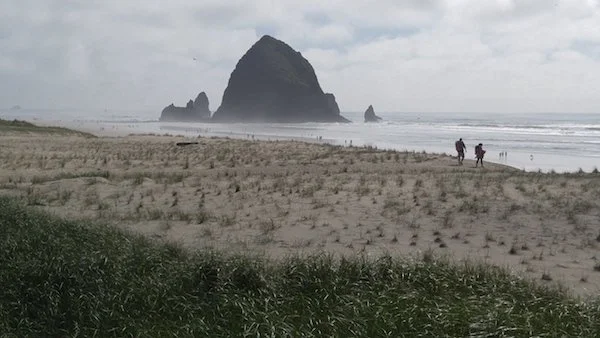 Two people walking along the sandy beach near Haystack Rock.