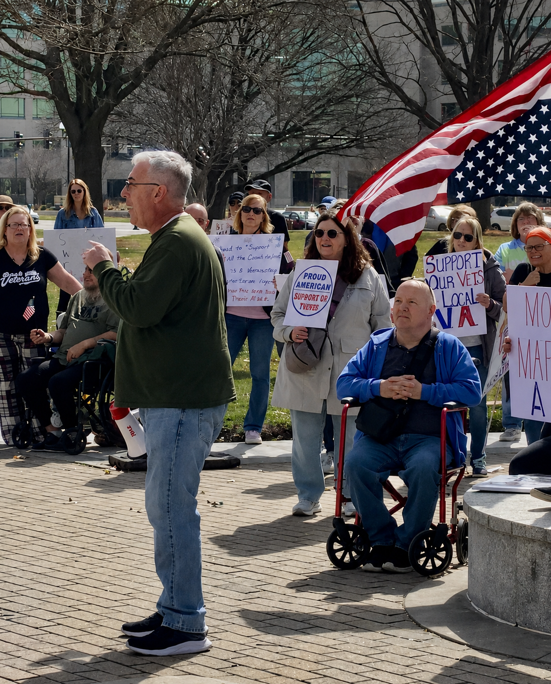 Robert Collins speaking to a group of veterans holding signs and flags at an outdoor rally at the steps of the Topeka, Kansas Capitol Building.