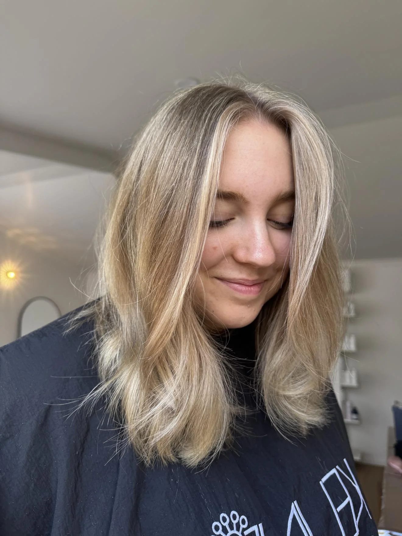 Close-up of a smiling young woman with blonde hair and closed eyes, indoors with a neutral background.