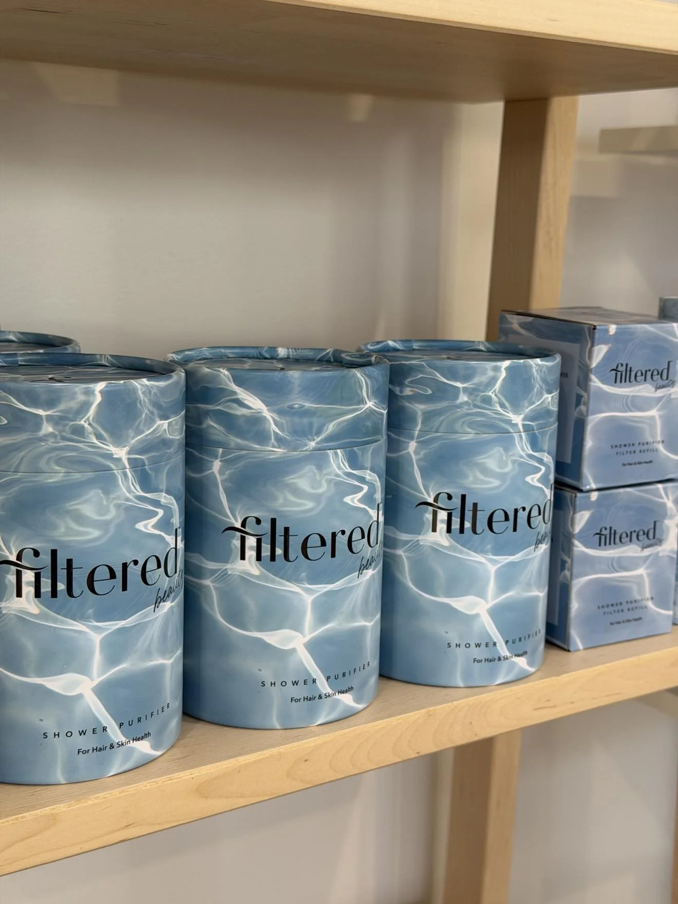 Several cans of filtered shower water purifier on a wooden shelf with a water ripple design and black text.