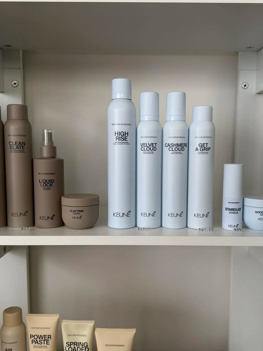 Shelf of KEUNE hair care products, including bottles labeled High Rise, Velvet Cloud, Cashmere Cloud, and Get a Grip, along with smaller containers and tubes.