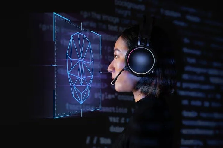 Woman wearing a black headset with microphone, looking at a digital screen displaying a geometric facial recognition graphic.