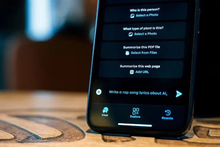 Smartphone screen displaying options for identifying a person, plant, or web page; writing rap lyrics about AI; with chat, explore, and recents icons at the bottom.