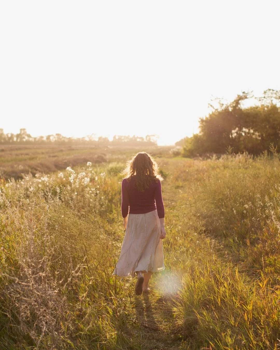 Woman walking through sun-kissed field in a white skirt