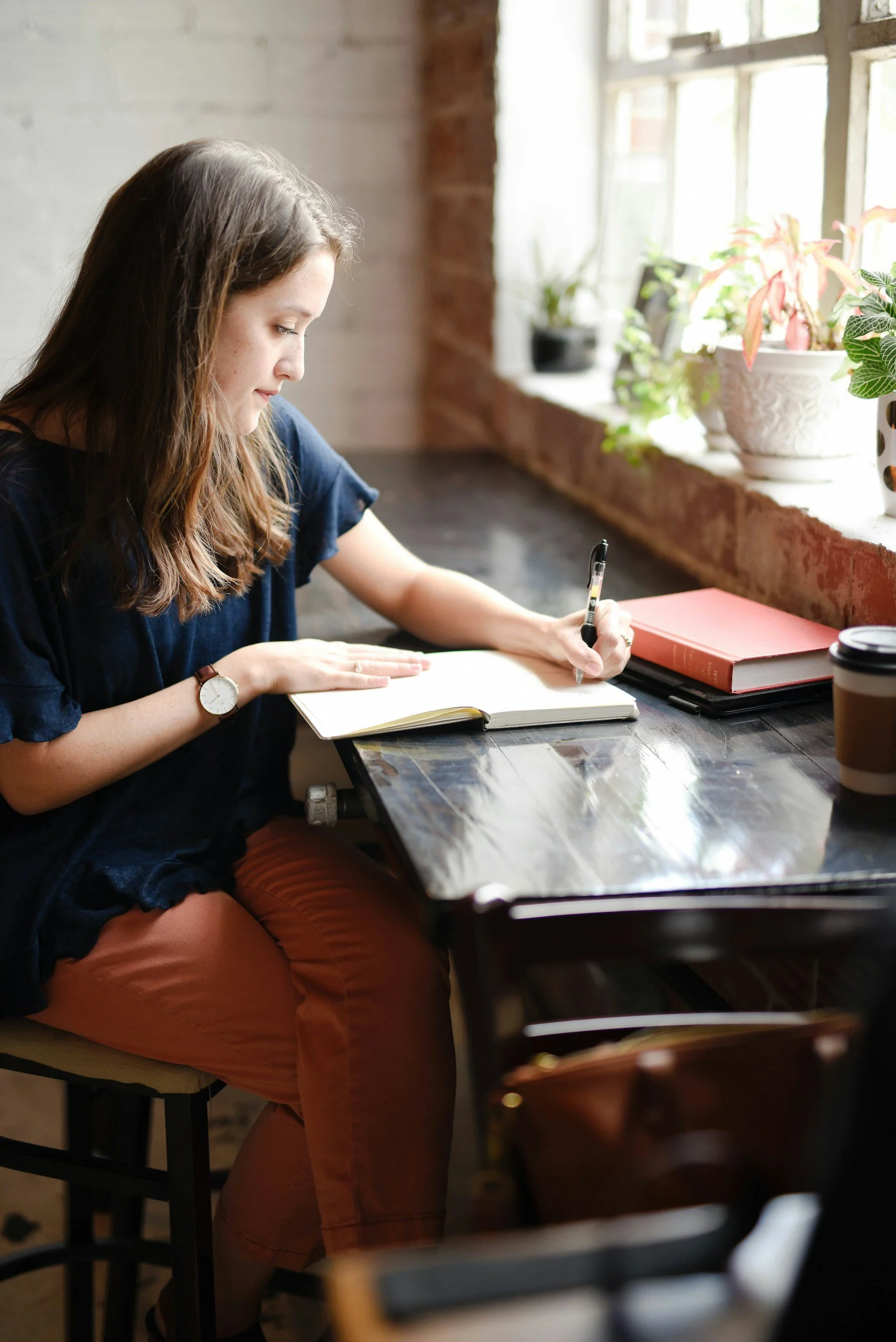 A woman working at a desk by a window, writing in a notebook